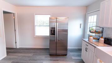 A modern kitchen with a stainless steel refrigerator, a window with blinds, and a countertop with kitchenware.