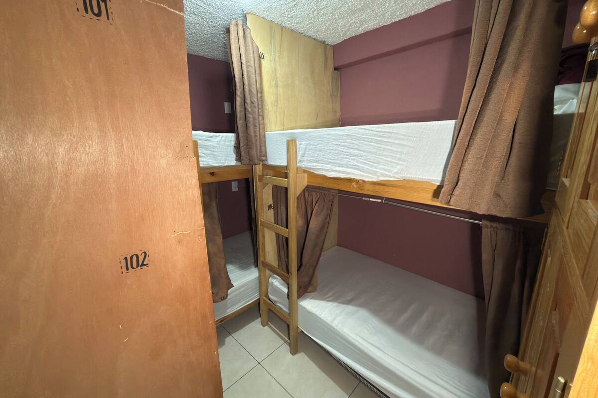 A dormitory room with bunk beds, numbered doors, and a tiled floor.