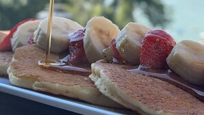 Un plato de desayuno con panqueques, fresas y plátanos con jarabe.