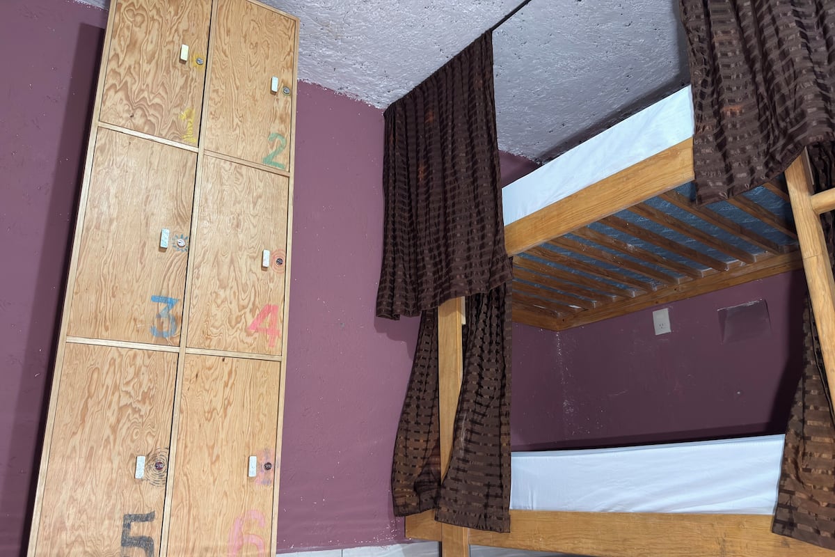 A room with a bunk bed, a wooden wardrobe with numbered compartments, and a purple wall.
