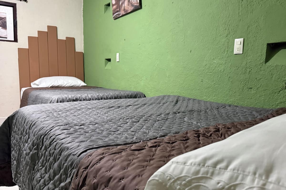 A room with two beds, a green wall, and a wooden headboard.