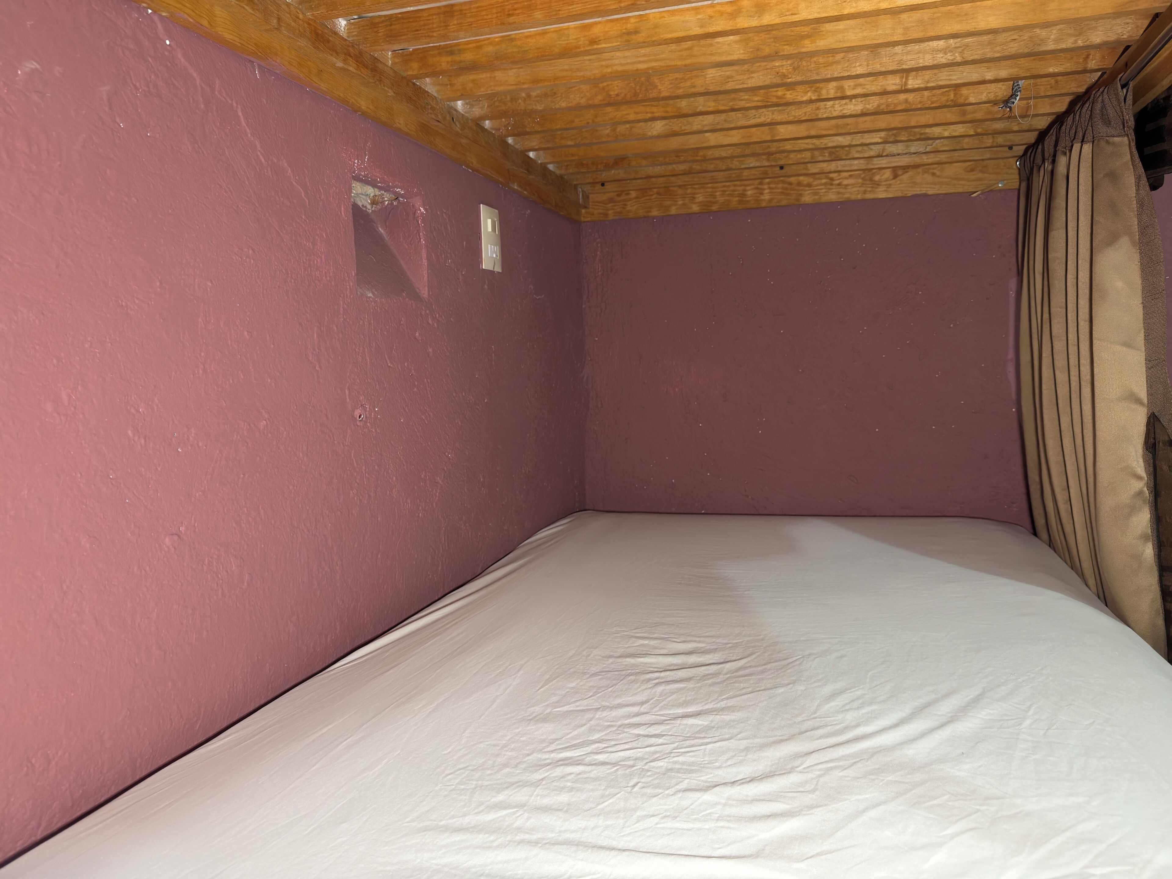 Une pièce avec un plafond en bois, un lit simple avec une literie blanche et un mur violet.