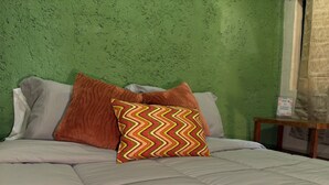Una cama con un cojín estampado, una mesita de noche de madera y una pared verde con textura.
