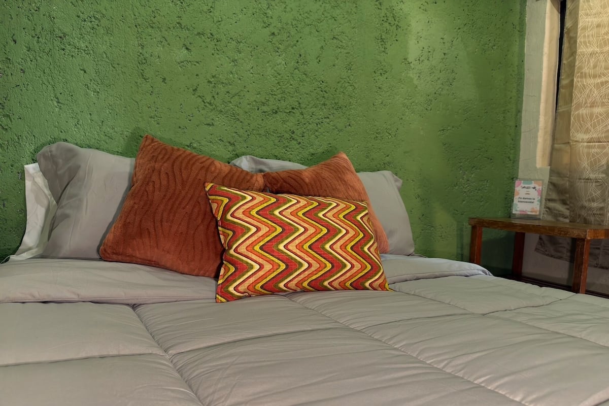 A bed with a patterned pillow, a wooden nightstand, and a green textured wall.