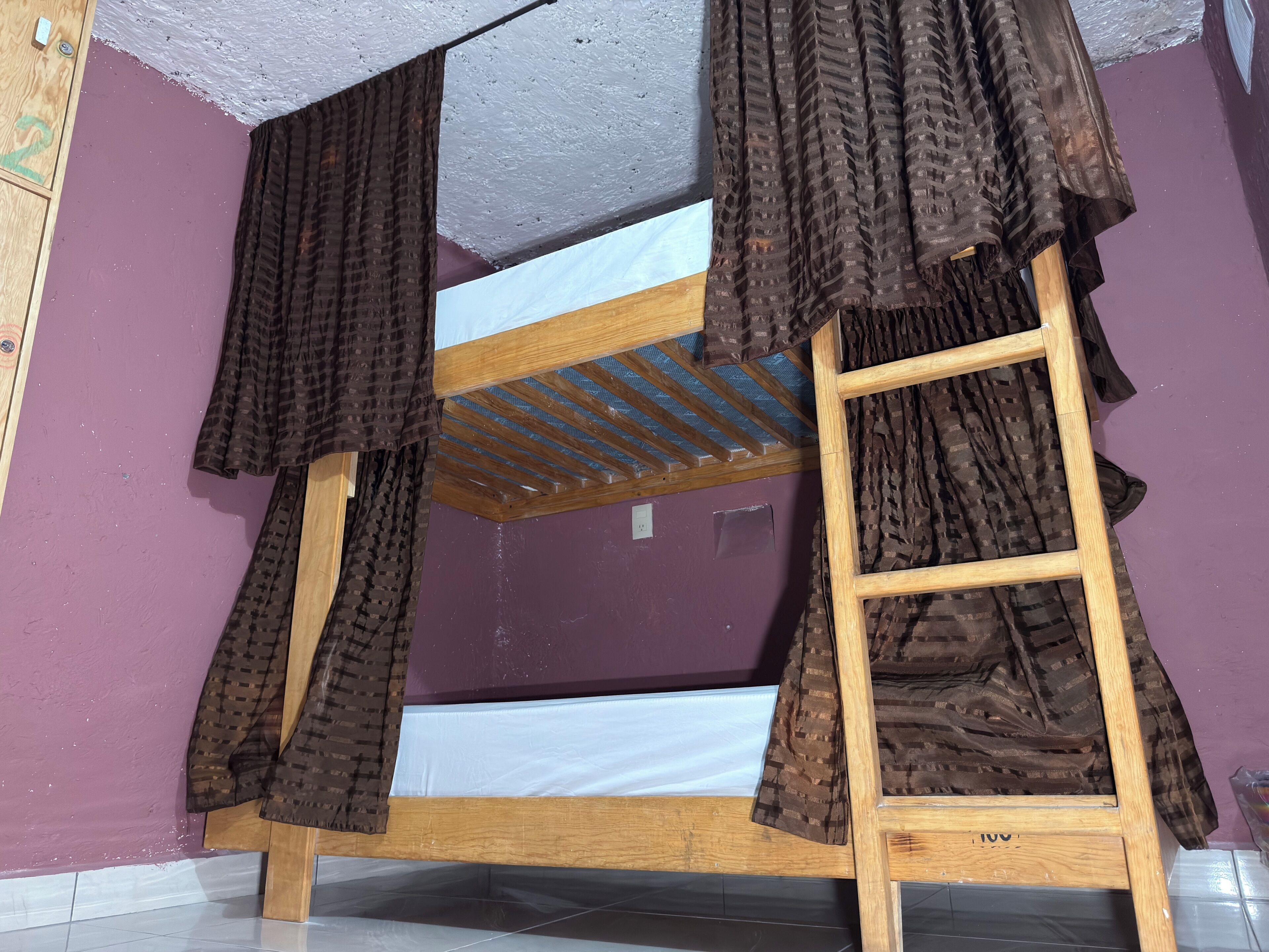 Una cama litera con estructura de madera, una escalera y un colchón.
