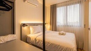 A hotel room with a bed, bedside table, and a window with curtains. - Easy Life Campus PUC by Xtay (Curitiba)