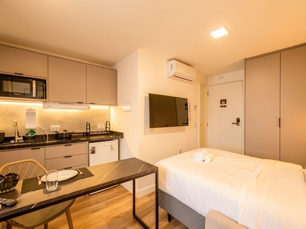 A compact hotel room with a kitchenette, a bed, and a TV.