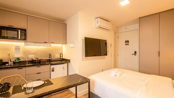 A compact hotel room with a kitchenette, a bed, and a TV.