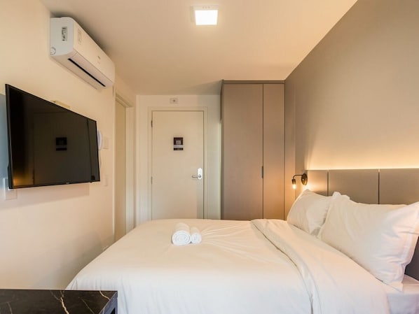 A hotel room with a bed, a flat-screen TV, an air conditioning unit, a door, and a light fixture. - Easy Life Campus PUC by Xtay (Curitiba)