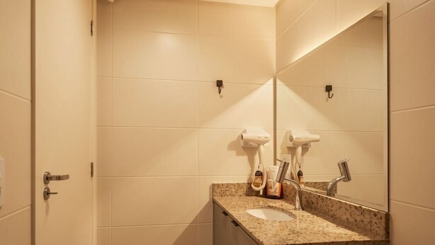 A bathroom with a sink, mirror, towel rack, and hairdryer. - Easy Life Campus PUC by Xtay (Curitiba)