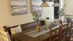A dining area with a wooden table, chairs, a bench, and two wall-mounted lamps. - 1 block from beach! 4bed 2bath Beachhouse. Just had a cancelation in July.  (Surfside Beach)