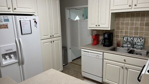 A kitchen with white cabinets, a refrigerator, a coffee maker, and a sign that says "At the Beach". - 1 block from beach! 4bed 2bath Beachhouse. Just had a cancelation in July.  (Surfside Beach)