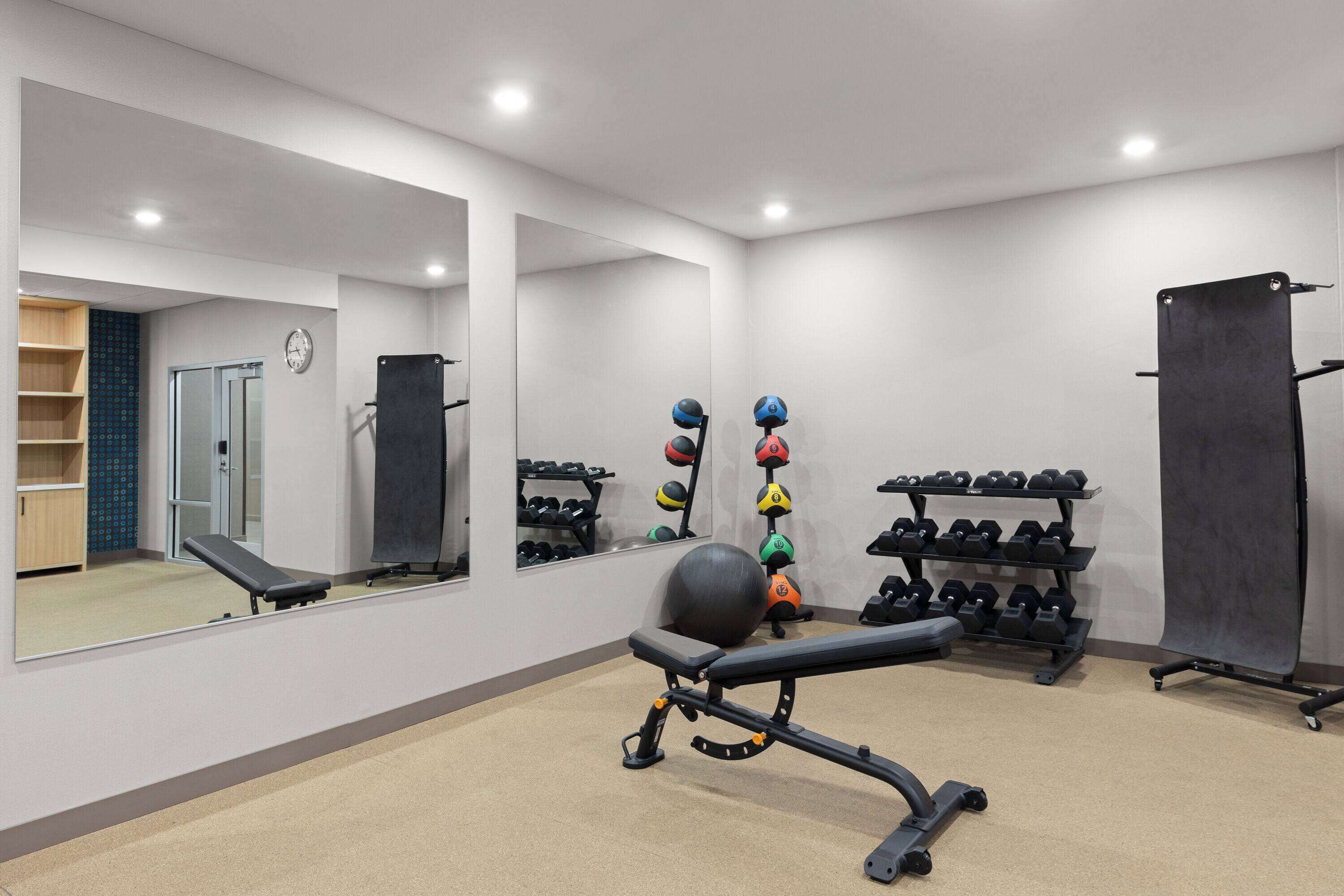 Een sportschool met trainingsapparatuur, een bank, een spiegel aan de muur en een deur naar een andere ruimte.