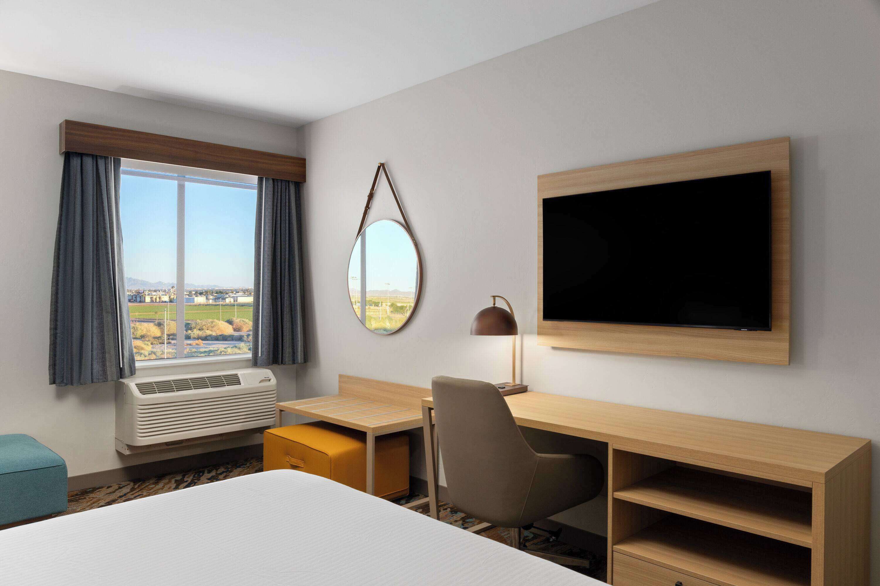 Une chambre d’hôtel équipée d’un lit, d’un bureau, d’une chaise, d’une télévision, d’un appareil de climatisation et d’une fenêtre avec des rideaux.