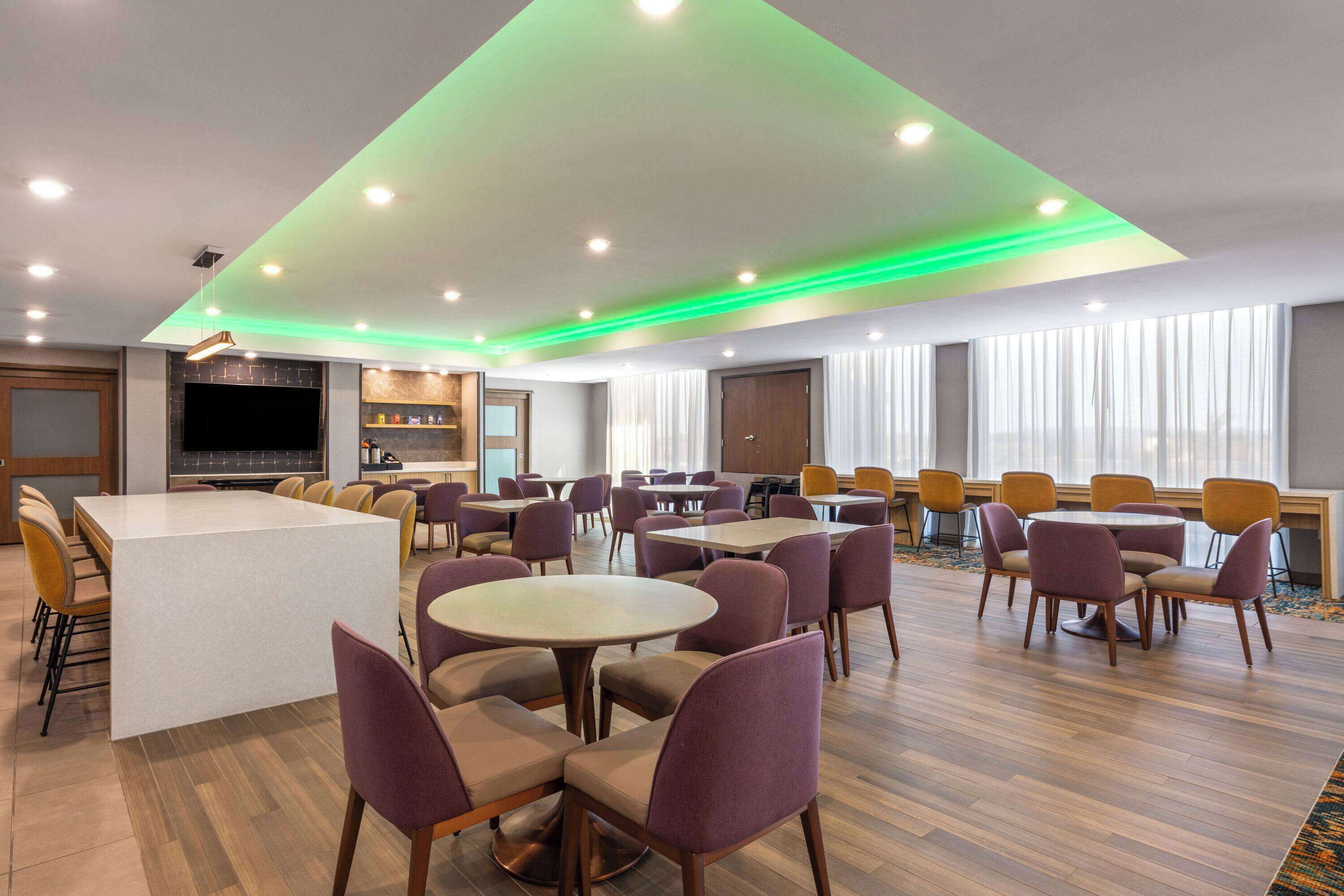 Un hall d’hôtel moderne avec un îlot central, plusieurs espaces de détente et une cuisine en arrière-plan.