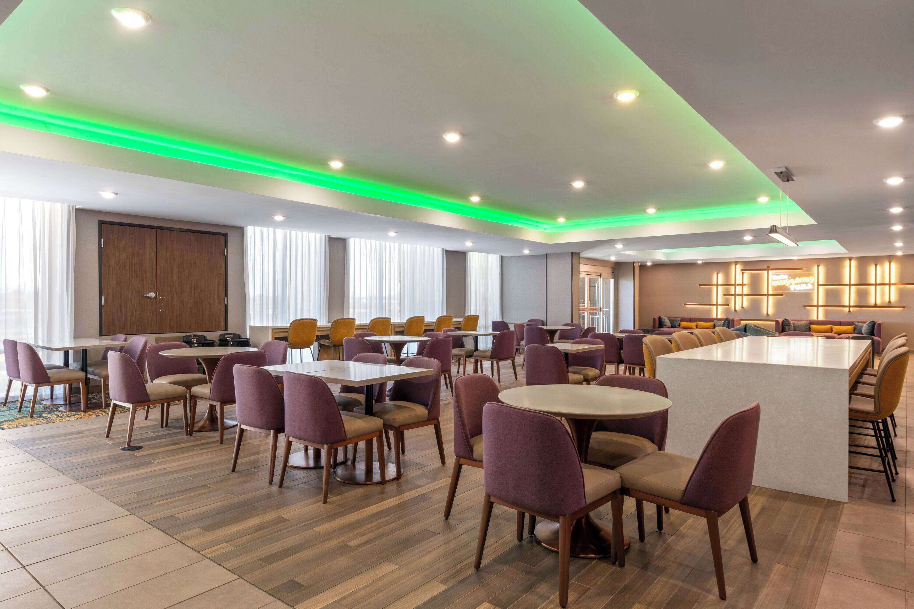 A spacious dining area with multiple tables and chairs, a central island, and a modern ceiling design with recessed lighting.