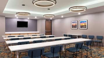 A conference room with long tables, chairs, a flat-screen TV, and ceiling lights.