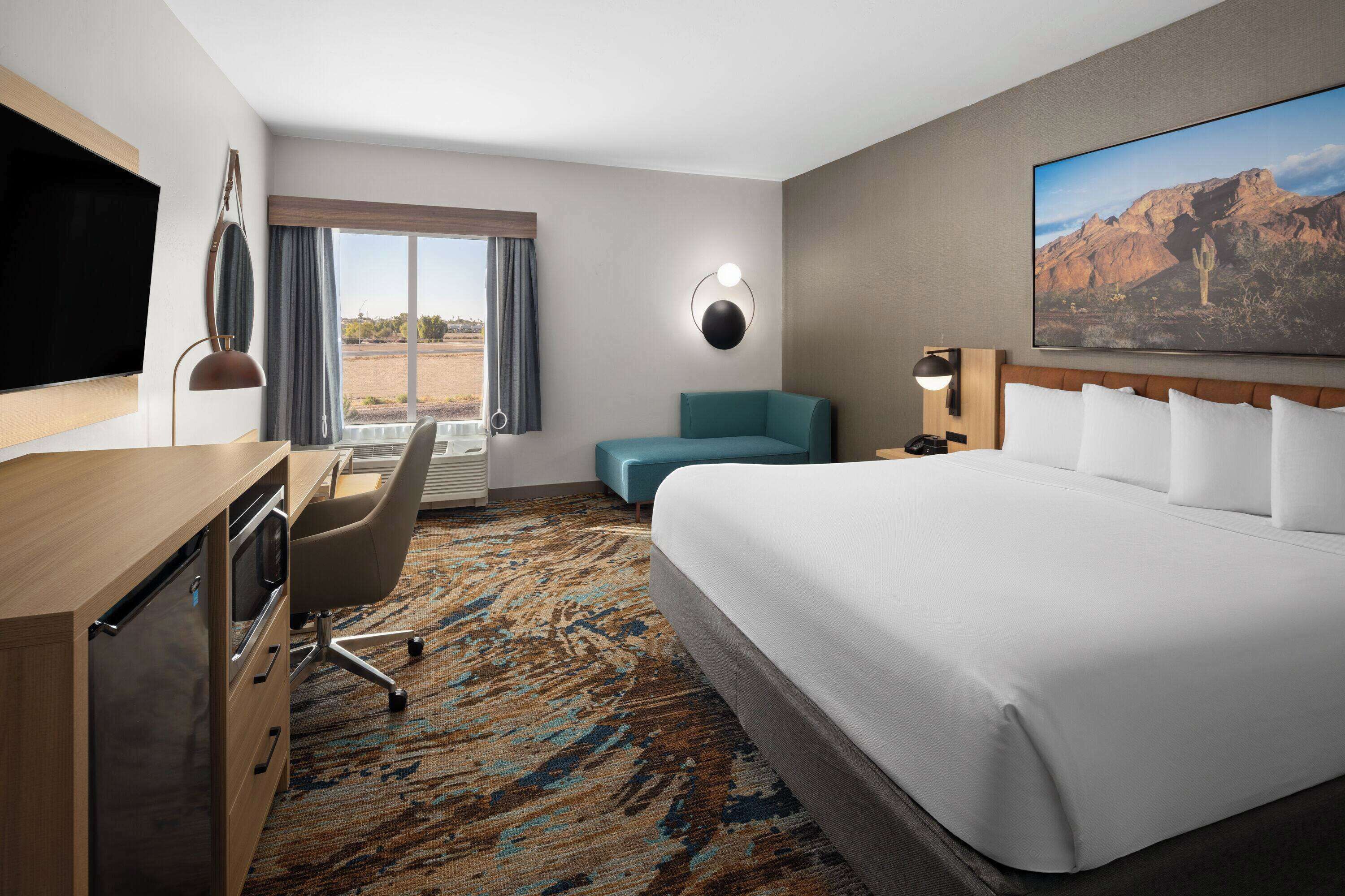 A hotel room with a bed, desk, chair, and a large window with curtains.