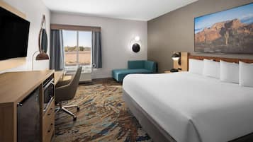 A hotel room with a bed, desk, chair, and a large window with curtains.