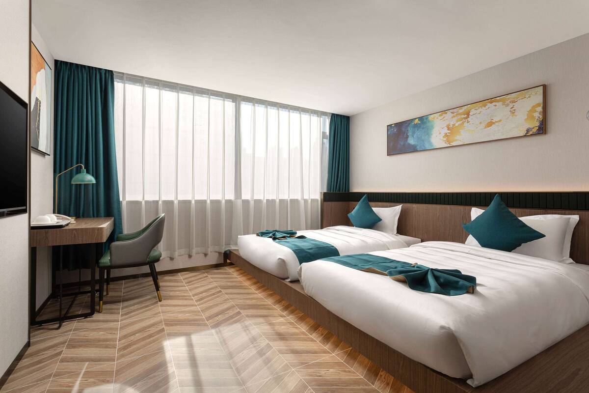 Une chambre d’hôtel avec deux lits, un bureau, une chaise, une télévision et une grande fenêtre avec des rideaux.