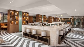 Un hall d’hôtel moderne avec un comptoir de réception en marbre, des étagères en bois ornées d’objets décoratifs et un sol à motifs géométriques.
