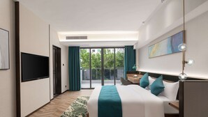 Une chambre d’hôtel moderne dotée d’un grand lit, d’un bureau, d’une télévision à écran plat et d’un balcon offrant une vue sur la verdure.