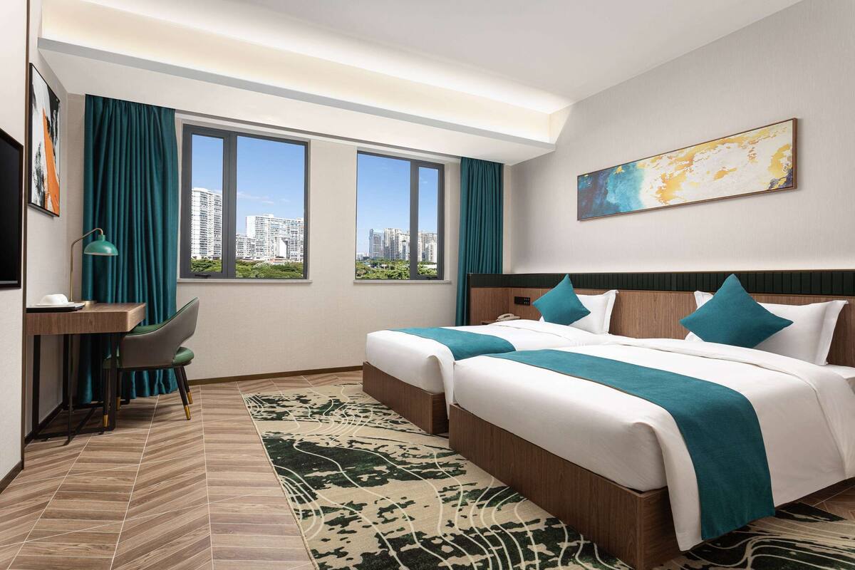 Une chambre d’hôtel avec deux lits, un bureau, une chaise et une grande fenêtre donnant sur la ville.
