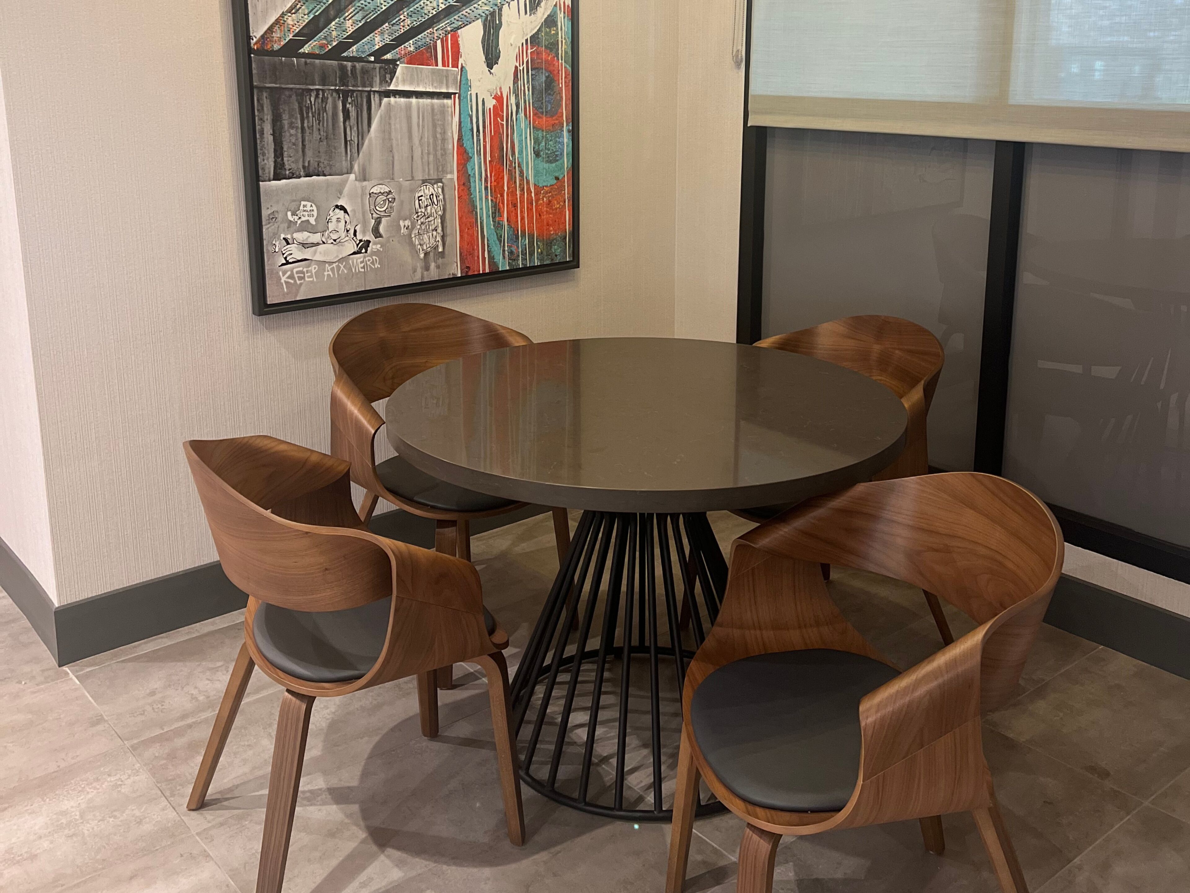 Une table ronde entourée de six chaises en bois, avec un pied en métal noir, et un tableau abstrait aux couleurs vives accroché au mur.