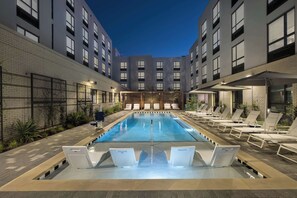 A swimming pool with lounge chairs and a poolside area, surrounded by modern buildings with large windows. - Hampton Inn by Hilton Austin East Side 5th Street (Austin)