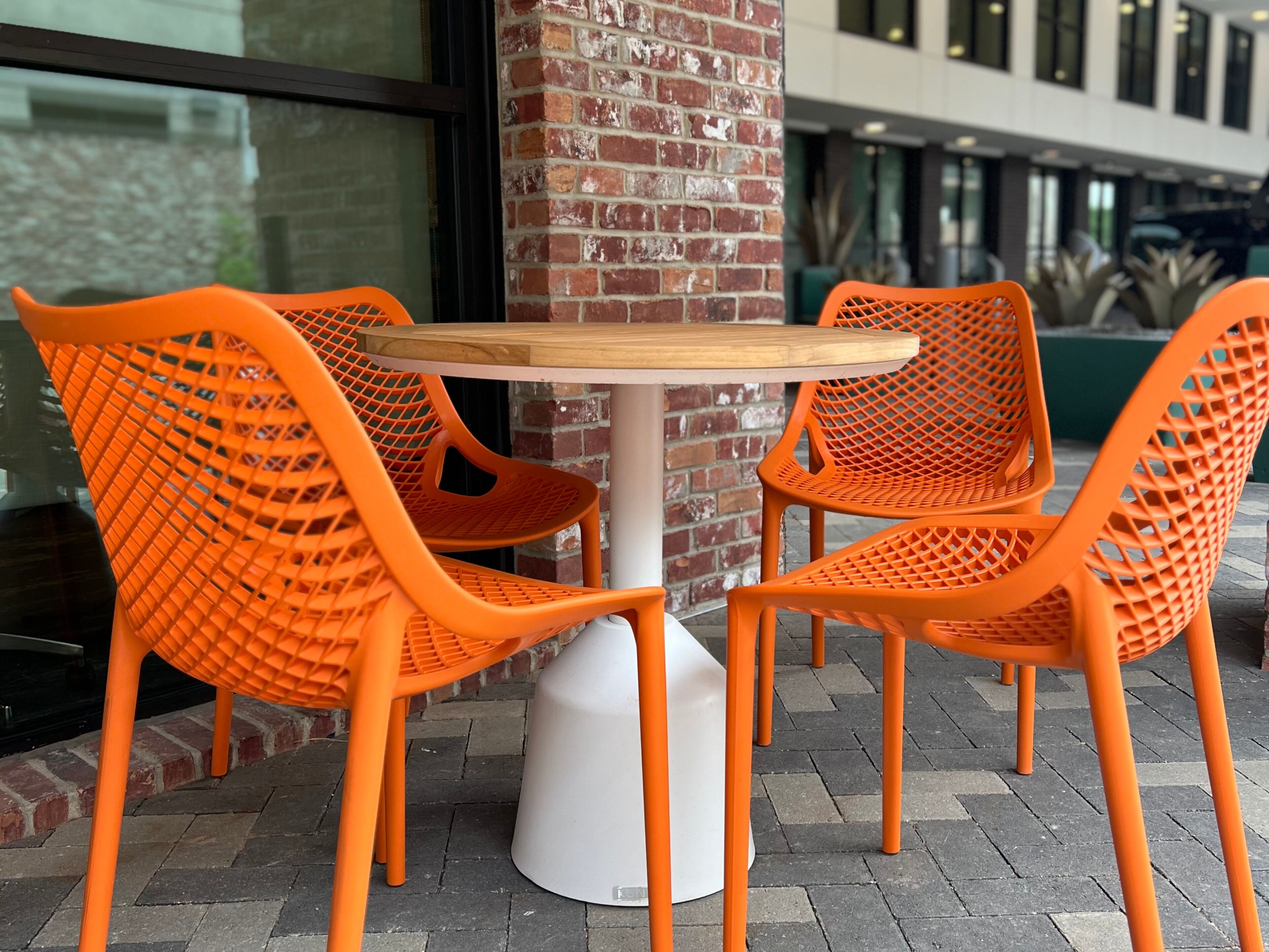 A table with four orange chairs, a white pedestal base, and a brick wall in the background.
