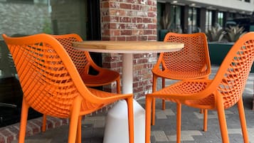 A table with four orange chairs, a white pedestal base, and a brick wall in the background.