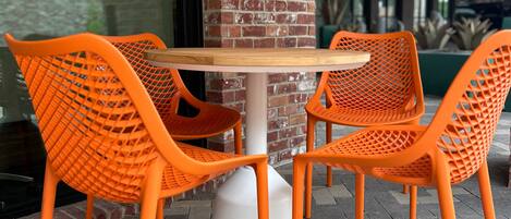 A table with four orange chairs, a white pedestal base, and a brick wall in the background.