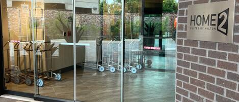 A hotel entrance with a glass door, a sign for 'HOME2 Suites by Hilton', and a brick wall.