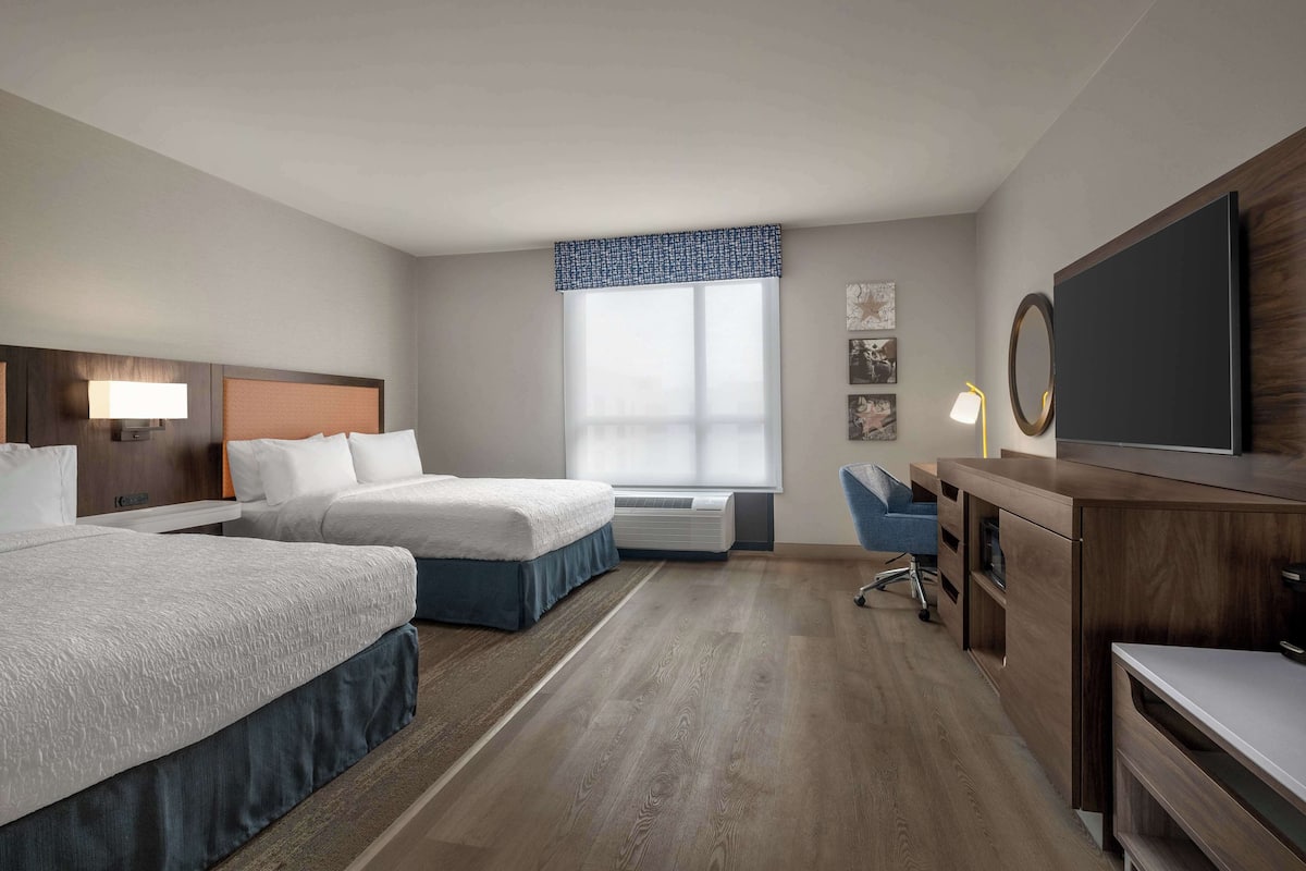 A hotel room with two beds, a desk, a TV, and a window with a view.