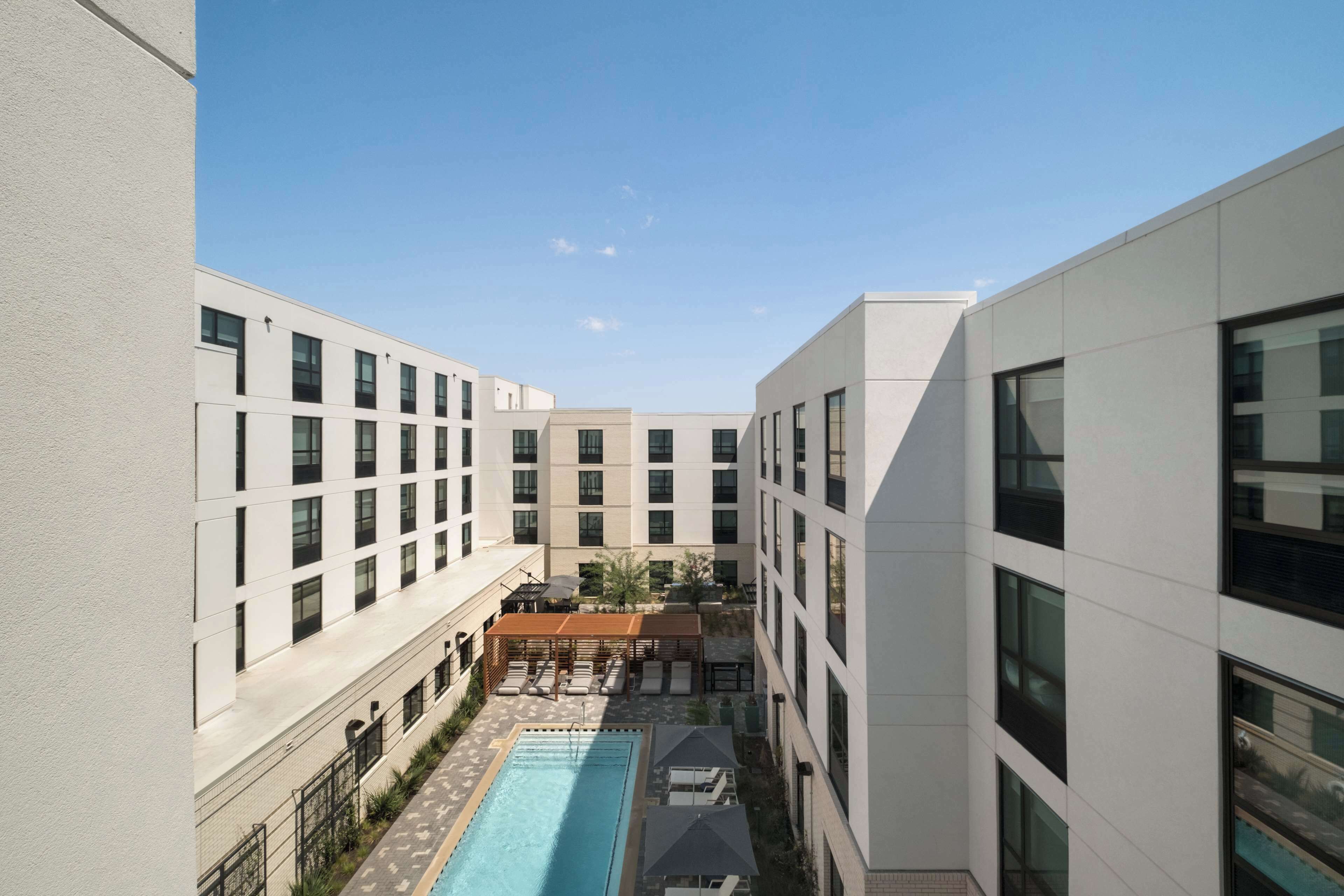 A modern building with a central courtyard featuring a swimming pool, lounge chairs, and a covered seating area.