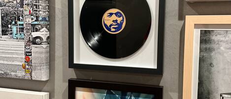 A framed vinyl record with a blue and yellow design, a framed photograph of a cityscape, and a framed picture of a plant.