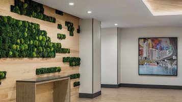 A modern lobby with a wooden wall adorned with green moss, a framed cityscape painting, and a wooden bench.
