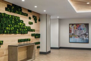 A modern lobby with a wooden wall adorned with green moss, a framed cityscape painting, and a wooden bench. - Hampton Inn by Hilton Austin East Side 5th Street (Austin)
