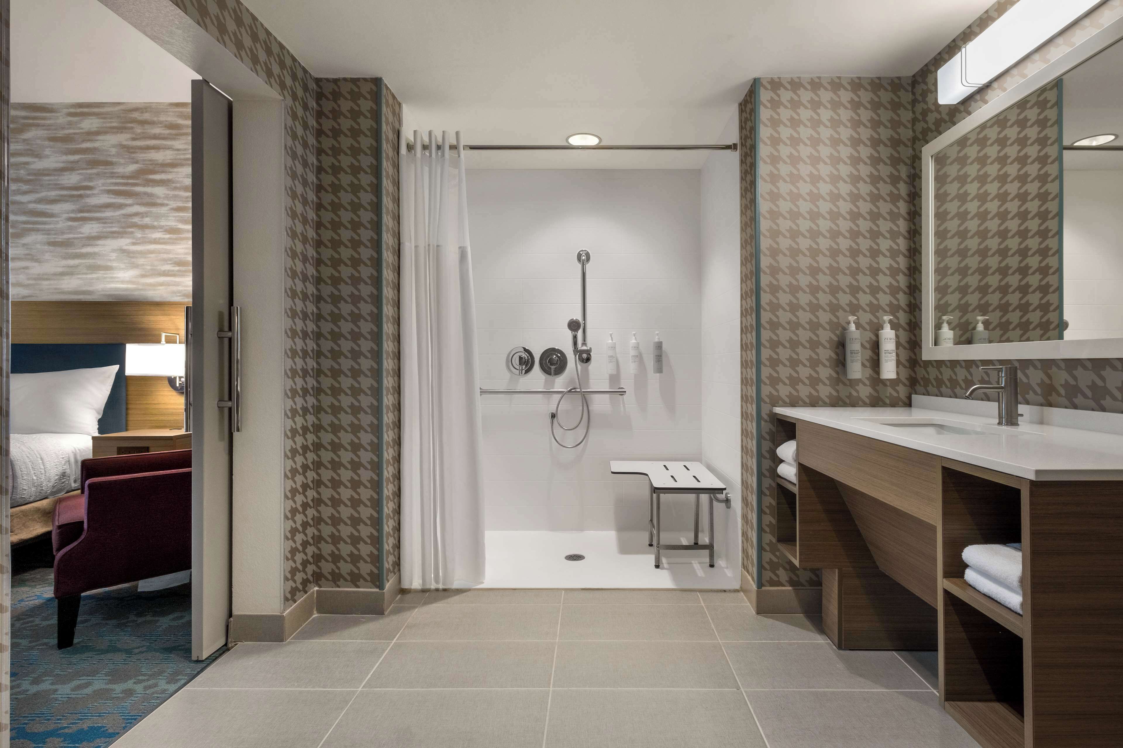Un baño de hotel moderno con ducha, tocador y un espejo grande.