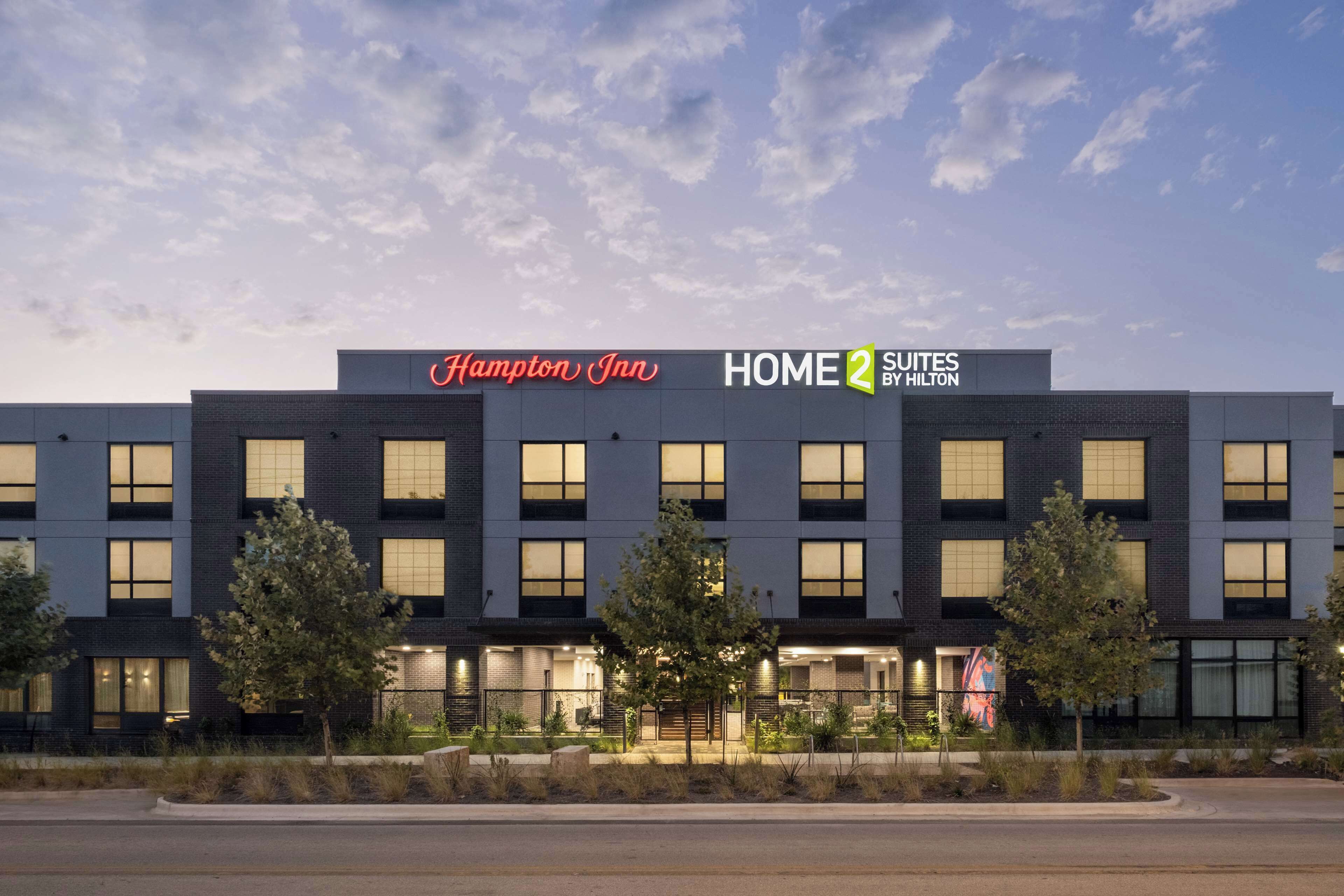 A modern hotel building with a sign for Hampton Inn and Home 2 Suites by Hilton.