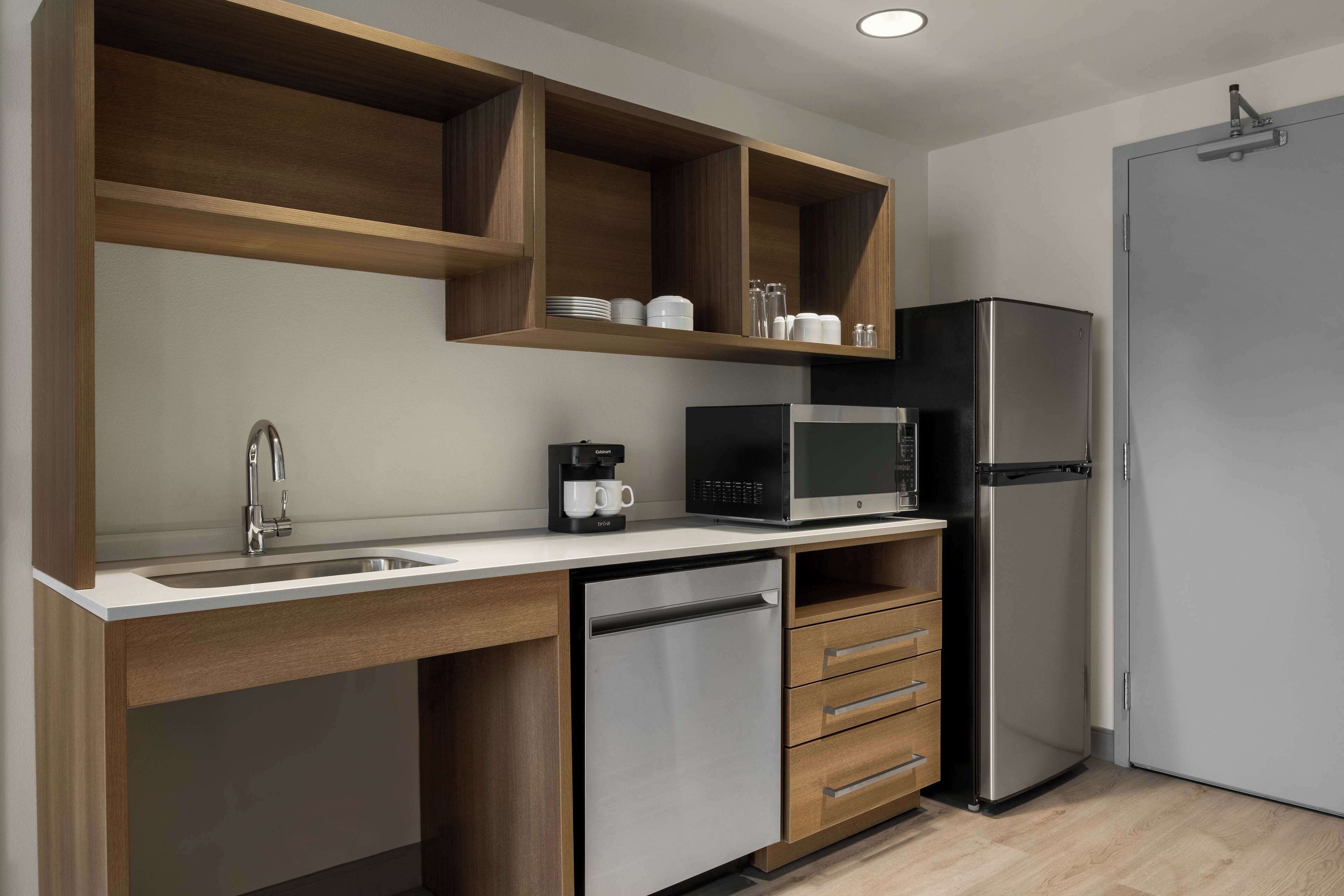 A modern kitchen with a stainless steel refrigerator, a microwave, a coffee maker, and wooden cabinetry.