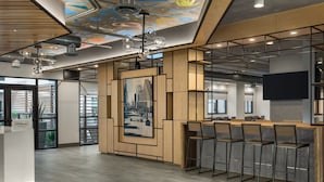 Un moderno vestíbulo de hotel con mostrador de recepción de madera, una obra de arte con motivo urbano y una zona de bar con taburetes altos.