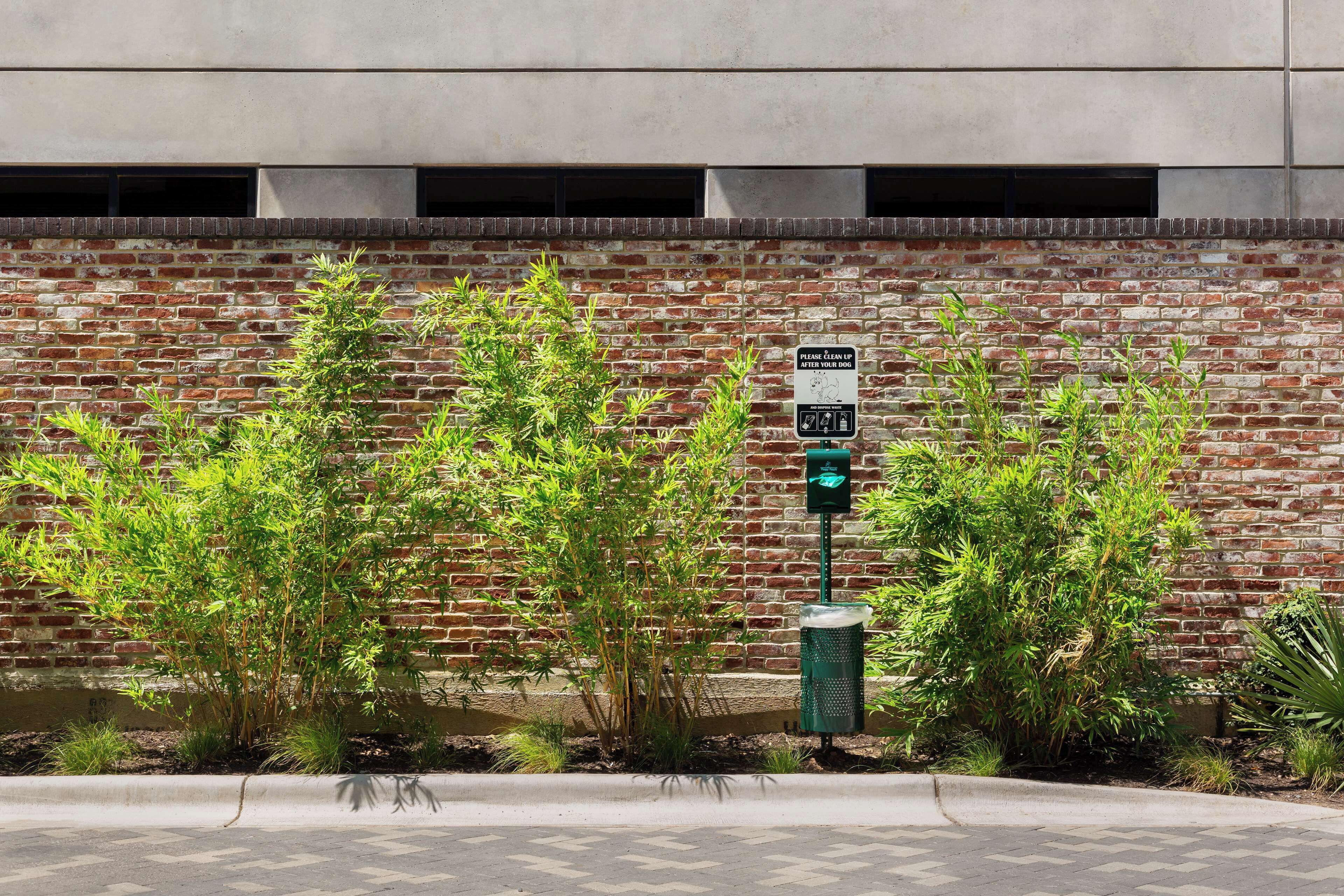 A brick wall with a green trash can and a recycling bin, and a sign indicating a parking area.