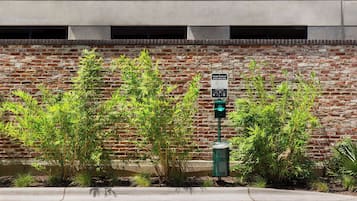 A brick wall with a green trash can and a recycling bin, and a sign indicating a parking area.