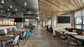 A modern restaurant with a long counter, multiple seating areas, and a kitchen in the background.
