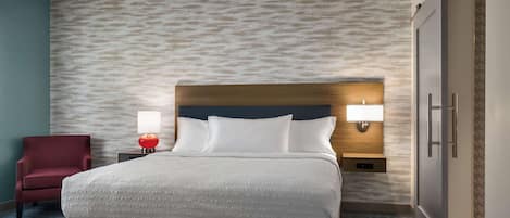 A hotel room with a bed, a nightstand, a lamp, a chair, and a wardrobe.