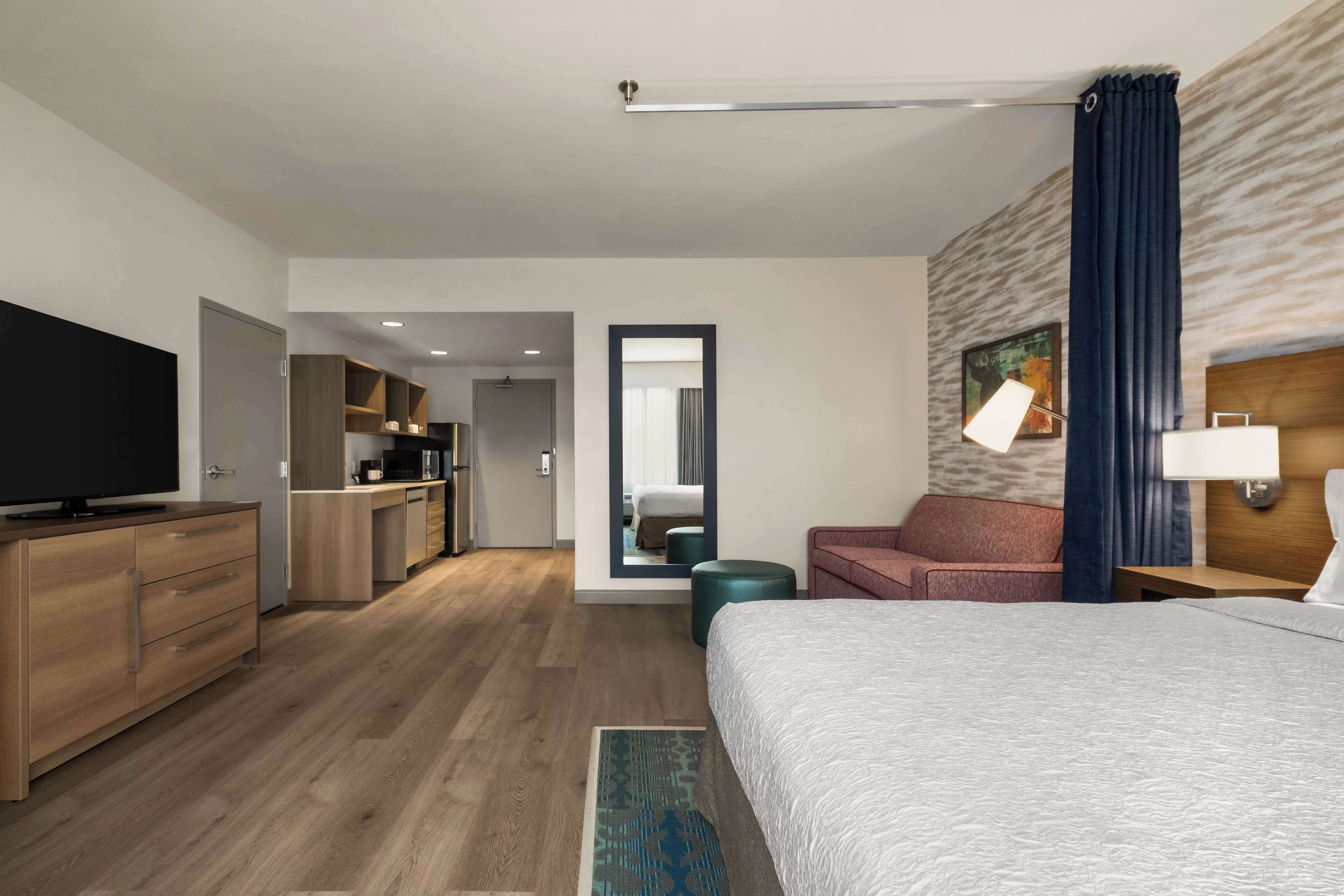 Een moderne hotelkamer met een groot bed, een televisie, een bureau en een kitchenette.