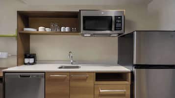 Una cocina compacta con microondas integrado, refrigerador de acero inoxidable, lavavajillas y cafetera sobre la encimera.