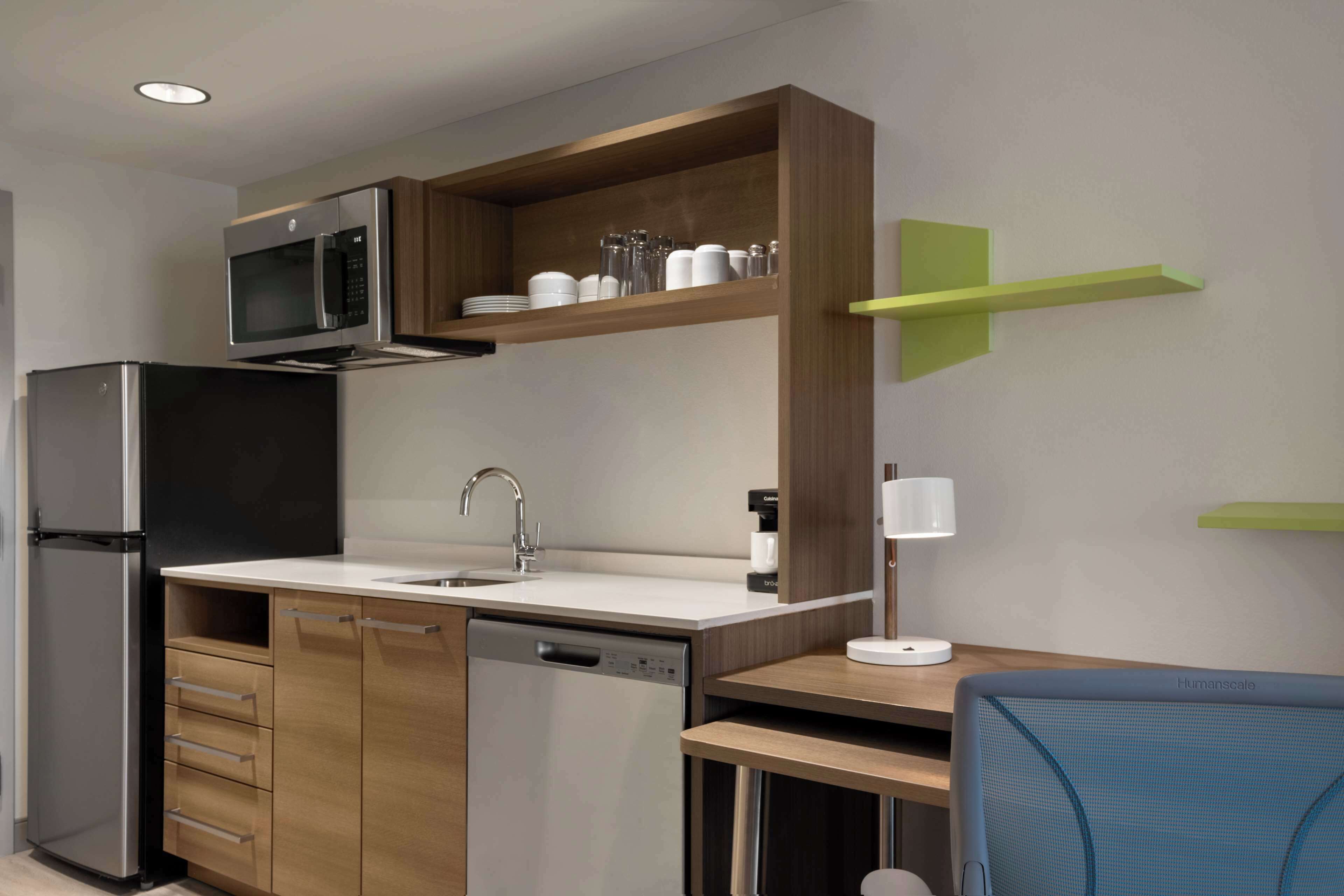 A modern kitchen with a built-in microwave, stainless steel refrigerator, and dishwasher. There is a wooden countertop, a sink, and a green shelf above the counter.