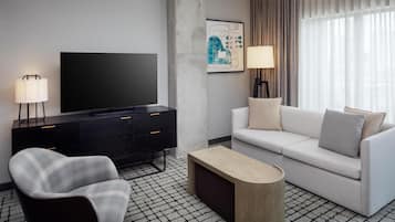 Una habitación de hotel moderna con una televisión de pantalla plana, un sofá, una silla, una mesa de centro y un mueble negro.